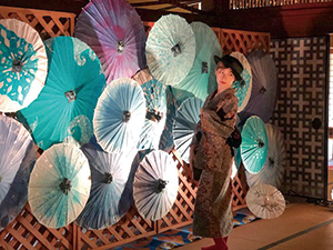 装飾された和傘の前でポーズをとる和洋装のモデルの写真