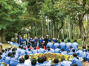 笹川邸ガーデンで演奏をする味方中学校吹奏楽部とそれを聞く生徒たちの写真