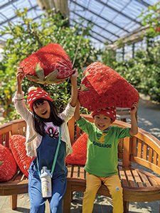 女の子と男の子がベンチに座り、作り物のイチゴを頭の上
に掲げている写真
