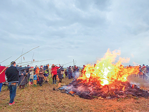 大勢の人が炎の燃え盛るどんと焼きを見守っている写真。