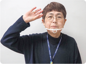 手話通訳者・鈴木さんが軽く開いた右手のひらを右耳の脇に上げている写真