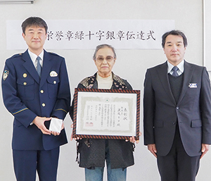 表彰状を持ち警察官とともにこちらを向いている渡辺キヨさんの写真