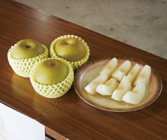 テーブルに３つの幸水梨とくし形に切って皮を剥かれた幸水梨が丸い陶器の皿に並べられた写真