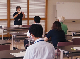 手話通訳者・鈴木さんが職員を前に手話を教えている写真
