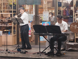 新飯田商店街のアーケードでフルートを吹く白南中学校・斎藤隆教頭先生とピアノを弾く稲村直輝先生の写真
