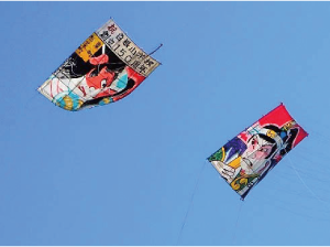 6畳の大きさの子供凧が飛んでいて、凧に描かれた人物の絵がお互いに見合っている写真