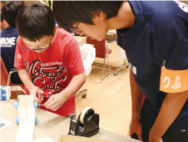 白根高校の男子生徒が、男の子に工作の作業方法を教えている写真