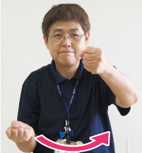 手話通訳者・鈴木さんが両手を「グー」にして片方は稲を握るように、もう片方はその稲を刈るように右から左に動かしている写真