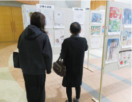 女性2人が「南区家族ふれ愛月間」出展作品を見ている写真