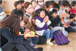 小さな子どもたちが、お父さん・お母さんの膝に座り笑顔でコンサートを見ている写真
