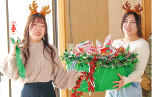新潟県立大学子ども学科2年生2人がトナカイの角を付け、ソリに入ったお菓子を子どもたちにプレゼントしている写真