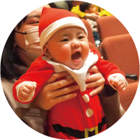 サンタの格好をした笑顔の赤ちゃんがお母さんに抱き上げられている写真