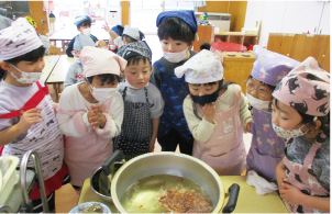 子どもたちが鰹節でだしをとっている大きな鍋を覗いている写真
