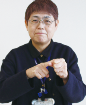 手話通訳者・鈴木さんが縦にグーにした親指に反対の手の人差し指を当てている写真