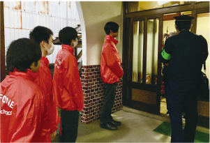 白根高校の生徒4人がオレンジの上着を着て、南警察署の警察官と一緒に防犯啓発のため戸別訪問をしている写真