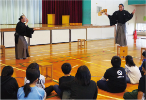 小林小学校で狂言師の大藏彌太郎さんと高木謙成さんが狂言「柿山伏」を披露している写　　　
　真