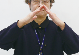 手話通訳者・鈴木さんが胸の前で両手の平を「ハ」の字に顔の前で広げている写真