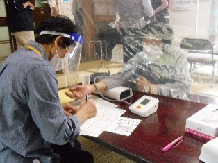 保健師が茶の間の利用者の血圧を測定している様子の写真