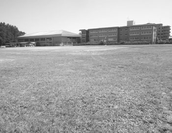 写真　旧二葉中学校グラウンド（中央区）。奥の建物は芸術創造村・国際青少年センター