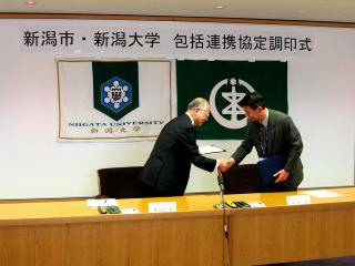 協定締結後に握手する篠田市長と長谷川学長