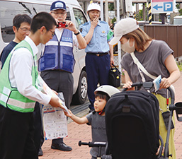 新津工業高校の生徒が親子連れに自転車盗難防止を呼びかけながら啓発品を配布している様子を撮った写真