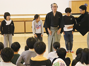 児童が狂言の指導を受ける様子を撮った写真