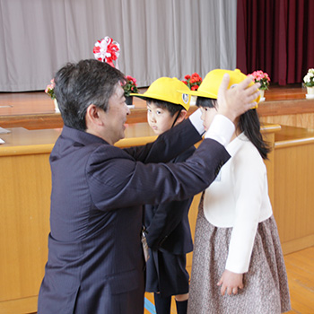 渡辺区長が新入生へ、交通安全帽(黄色い帽子)を贈呈