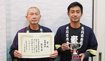 巻凧の、優勝の部で優勝した岩見会の2人が賞状とカップを持っている写真