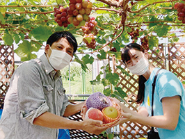 フルーツ童夢やまだ農園の山田さんと前田さんがフルーツの入ったかごを間に一緒に持っている写真