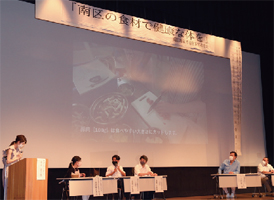 ステージ上、スクリーンに映る画像を見ながらトークショーをする川合俊一さんとトーク者たちの写真