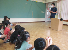 富山農園・富山喜幸（とみやまよしゆき）さんがプラムを持ち子どもたちに話をしている写真