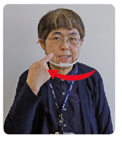 口を大きく開き歯を見せた手話通訳・鈴木さんがその人差し指を口の右端に動かしている写真
