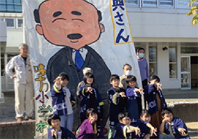 味方小学校6年生が「こうさん」「りょうじんさん」を描いた大凧の前で集合している写真
