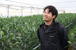 ふっくらと膨らんだつぼみを付けたユリの畝脇で内山太晴さんが斜め上に目線を上げ、笑顔の写真