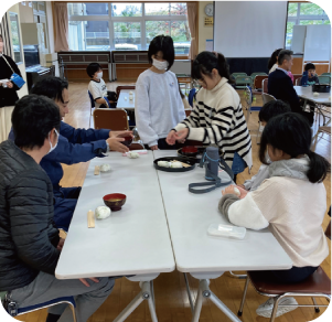 お盆に自分たちで育てた野菜で作った料理を運び、お世話になった地域の人たちに振舞っている写真