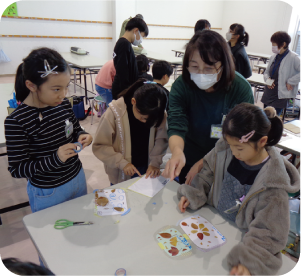 女の子３人が女性に教わりながら、植物を使ったアートシートを作成している写真