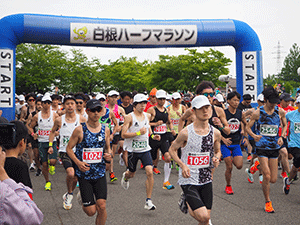白根ハーフマラソンと表示してある青いスタートゲートからスタートする選手たちの写真