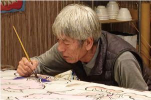 筆を持ち凧の下絵に真剣な表情で色塗りをする荏原さんの写真