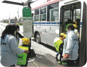 バスに乗り込む小学生を誘導する児童委員たちの写真