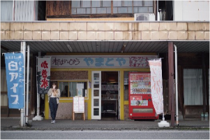 商店街の「やまとや」の前で女性が白アイスを食べている写真