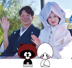 狸に扮した羽織・袴の心労とわたぼうしを被った新婦が手を振る写真