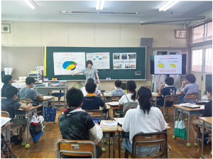 教室で児童が前を向き、講師の話を聞いている写真