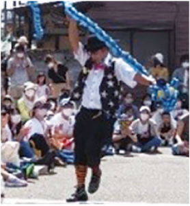 帽子に蝶ネクタイのパフォーマーが棒状の風船でパフォーマンスをしている写真