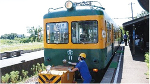 かぼちゃ電車の先頭に車両移動機を付け、発車前の点検をする整備士の写真