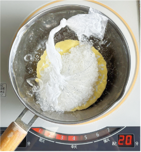 鍋に小皿を敷き、そこにコメと水が入った袋を乗せ加熱している写真