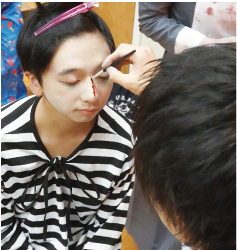 顔を白く塗り、傷を描いてもらっている男性の写真