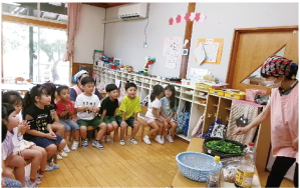 ホットプレートでピーマンを焼いているところをイスに座り、注目する園児たちの写真