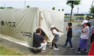 簡易の煙ハウスにハンカチで口を押えながら入るこどもたちの写真