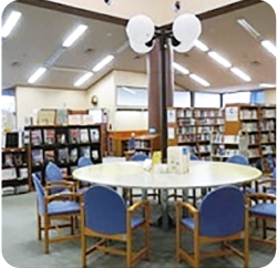 利用者用の大きな丸テーブルを真ん中に本棚が奥に並ぶ月潟図書館内の写真