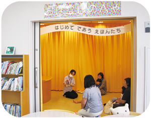 複数の女性がこどもを膝に乗せて座り、語り部の読み聞かせに聴き入っている写真